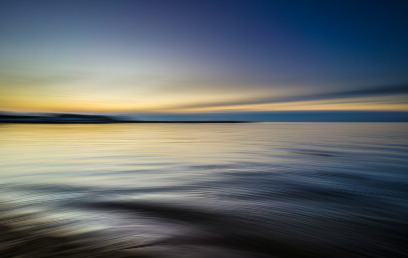 tranquil rippling waters reflect a blue and yellow sky at sunset, water sea calm and horizon 4k