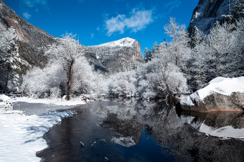 a melting stream in the mountains surrounded by snow covered trees against a bright blue sky, stream in winter mountains 4k