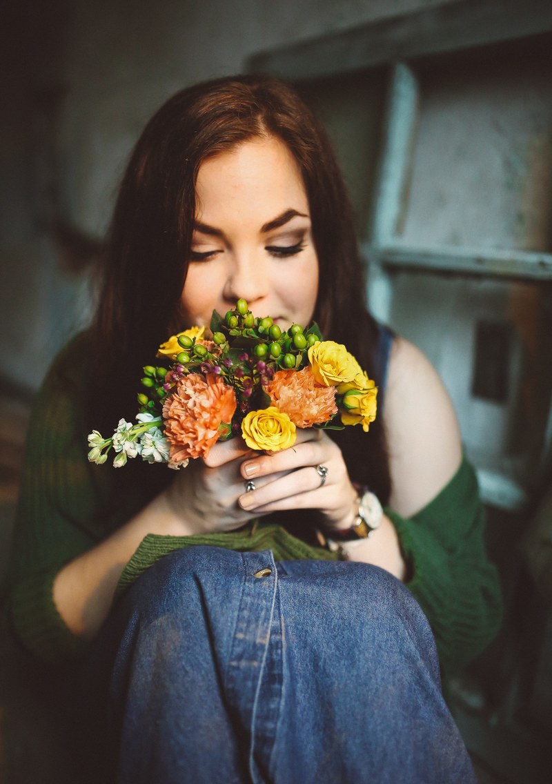 a young woman sitting on the floor and smelling a small bouquet of flowers, taking in the sweet scent 4k