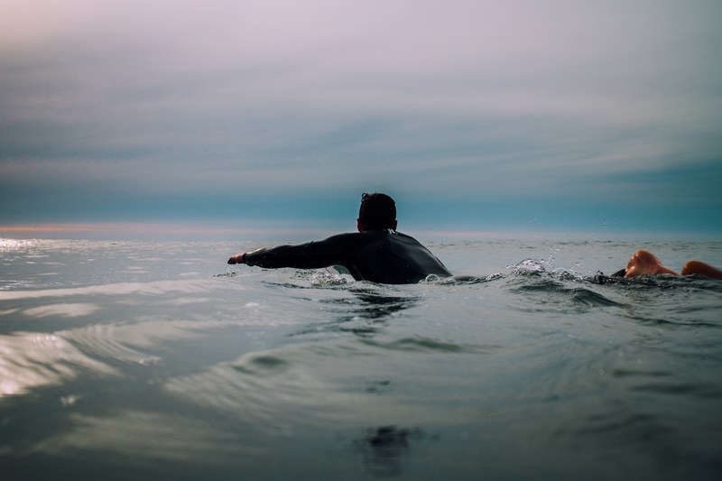 a male surfer swimming in a calm sea under a cloudy sky in raglan, paddle out 4k