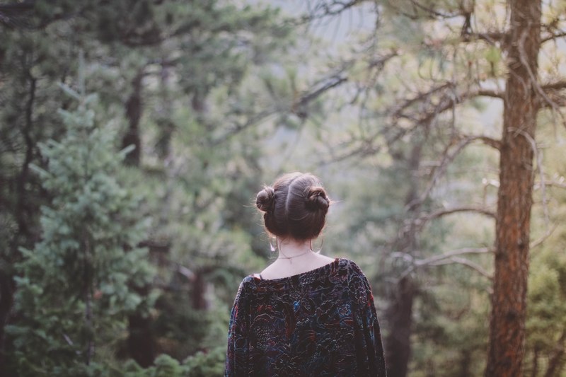 a woman with her hair up in buns walking through an evergreen forest, woman in the evergreen woods 4k
