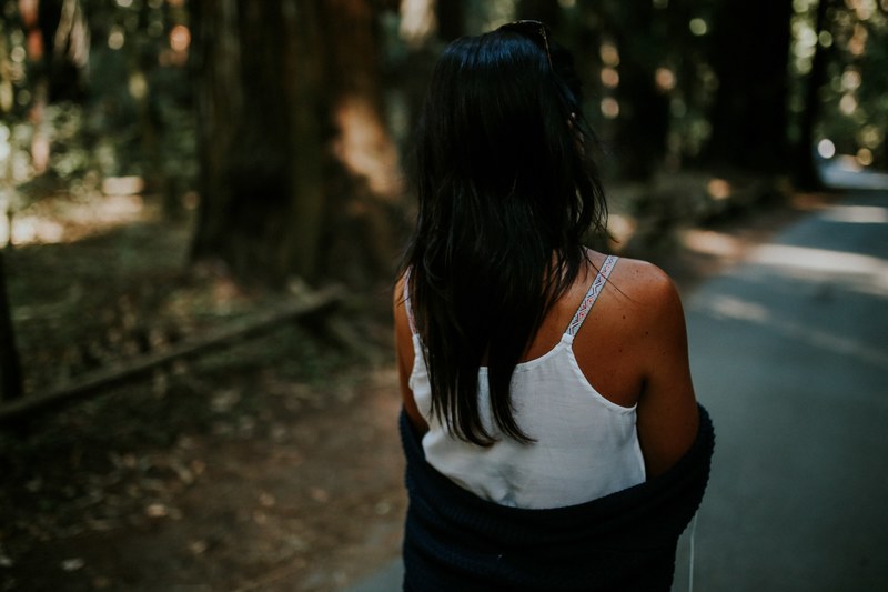 a dark haired woman walking across a path in the park in armstrong redwoods state natural reserve, a stroll in the park 4k