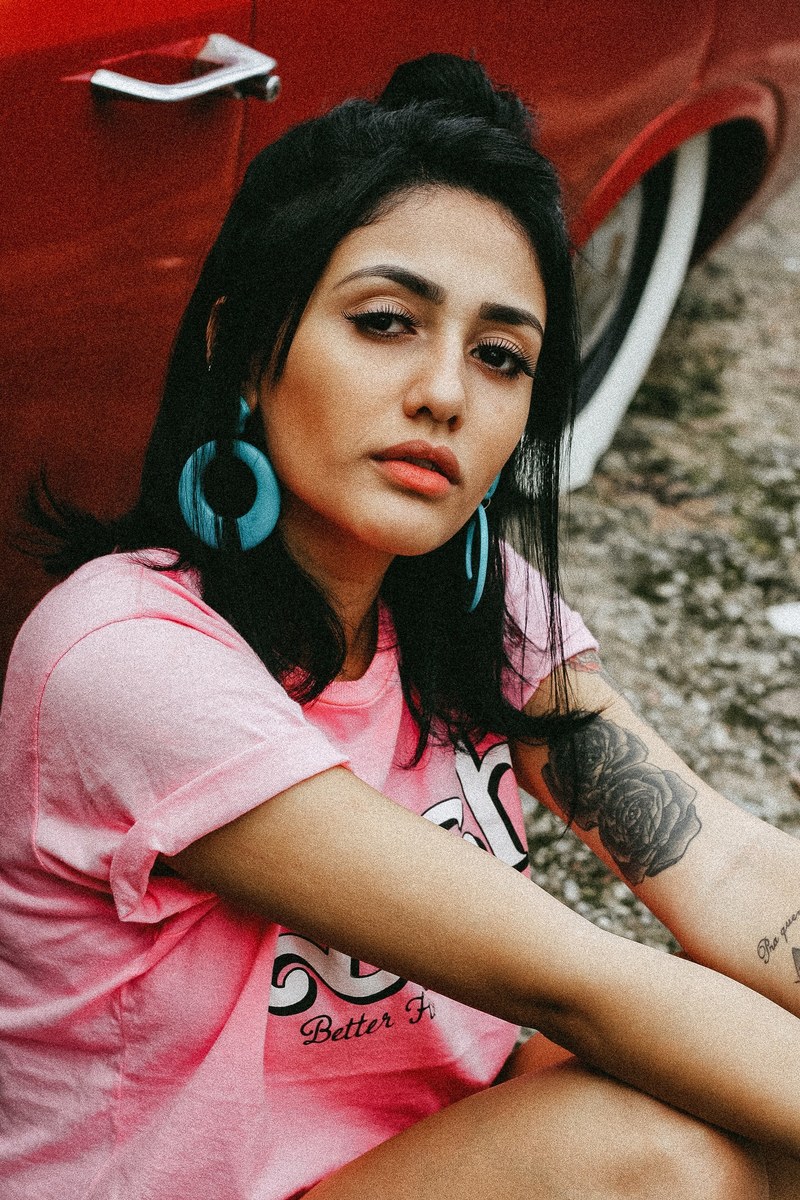 woman with hoop earrings and a pink tee shirt near a red car, drag racing chic 4k