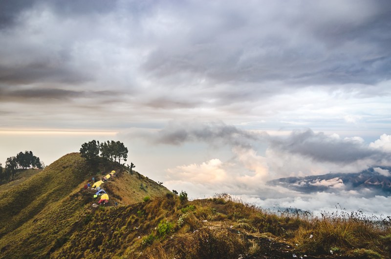 small tents on a grassy hill overlooking a mountainous landscape covered in clouds, camp on a hill near mount rinjani 4k