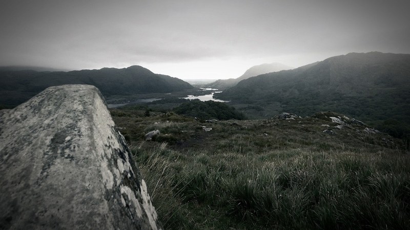 a colorless shot of a desolate hilly grassland with a rock partially obscuring the view, gloomy grasslands 4k
