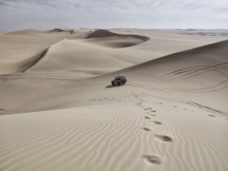 an off road vehicle driving on the desert with sand dunes stretching to the horizon, off road desert drive 4k