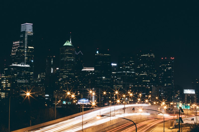 a long exposure shot of a freeway in philadelphia with light trails on the road and highrises at the back, philadelphia in the evening 4k