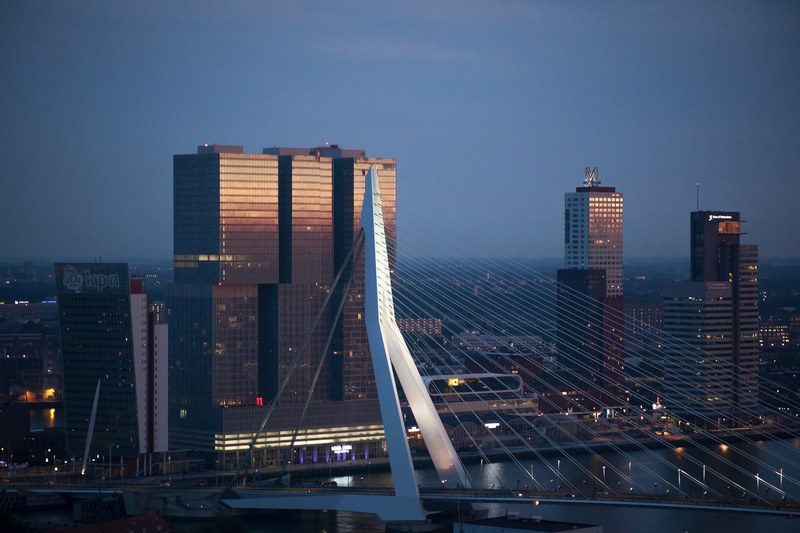 a bridge connecting two shores of a river in rotterdam with high rises on the bank, erasmus bridge at sunset 4k