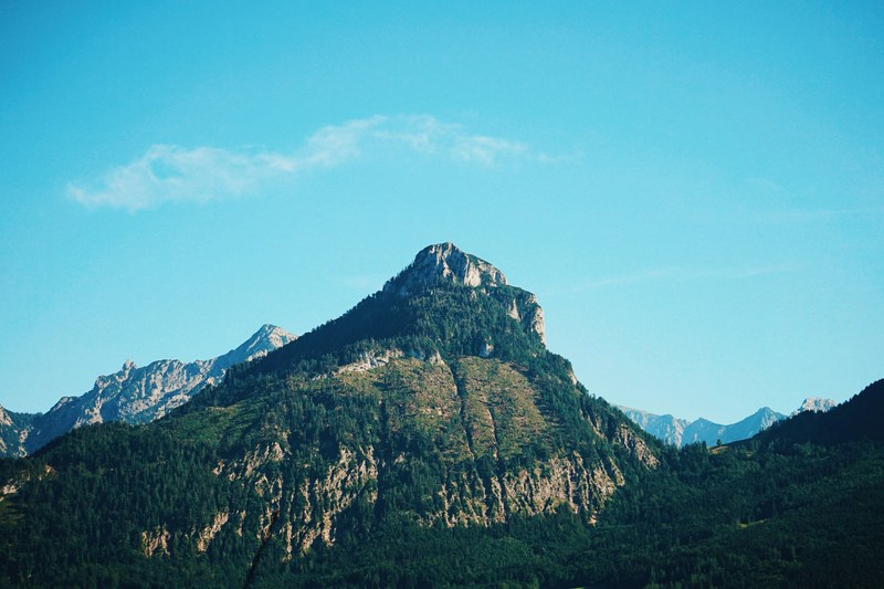 a lofty wooded mountain against a light blue sky, mountain peak near wolfgangsee lake 4k