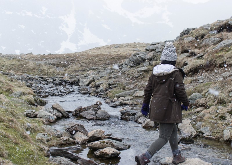 woman hiking across a stony stream on the grassy hills of helvellyn during snow, hiking woman helvellyn 4k