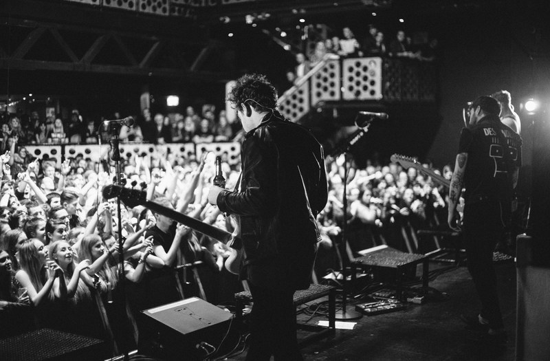 a black and white shot of a band on stage with rows of young fans in front of them, rock concert in black and white 4k