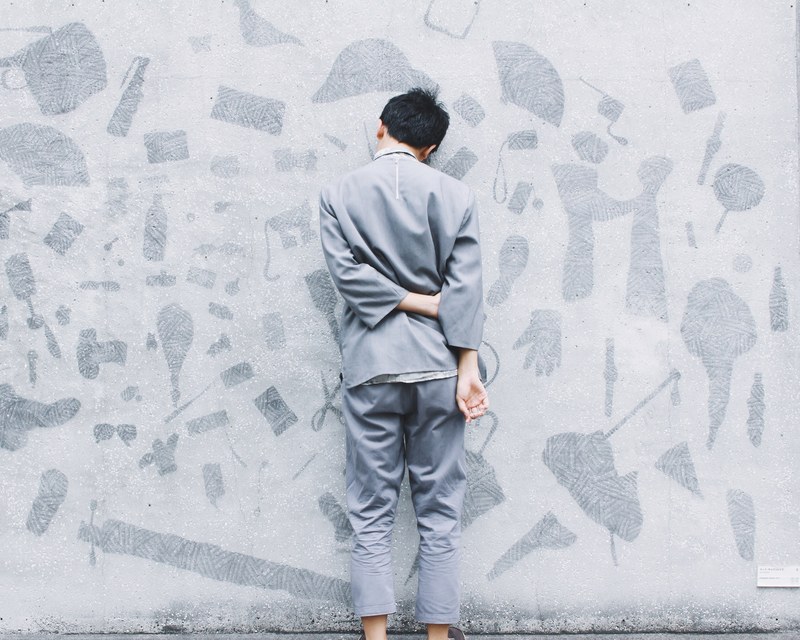 man wearing gray suit leans face first against gray wall with art, man leans against gray wall 4k