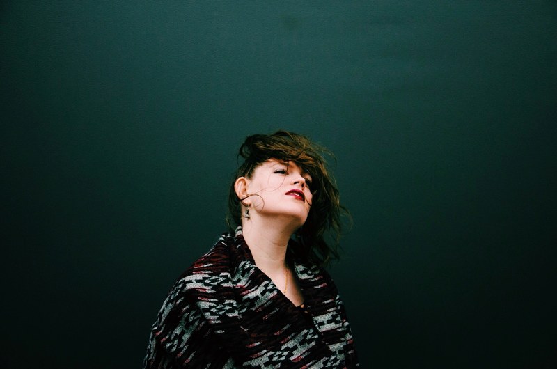 woman flips hair in the wind while standing against a dark wall, windy hair flip 4k