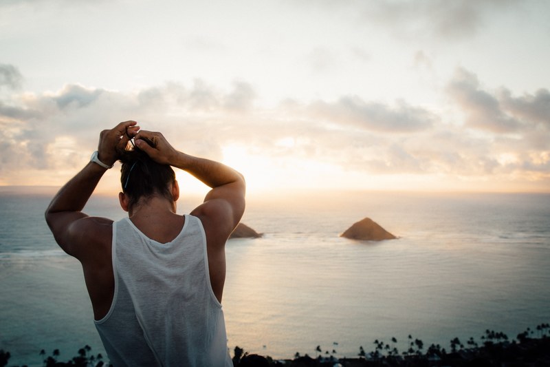 a man standing on a mountain by the coast putting his hair into a bun, man bun 4k
