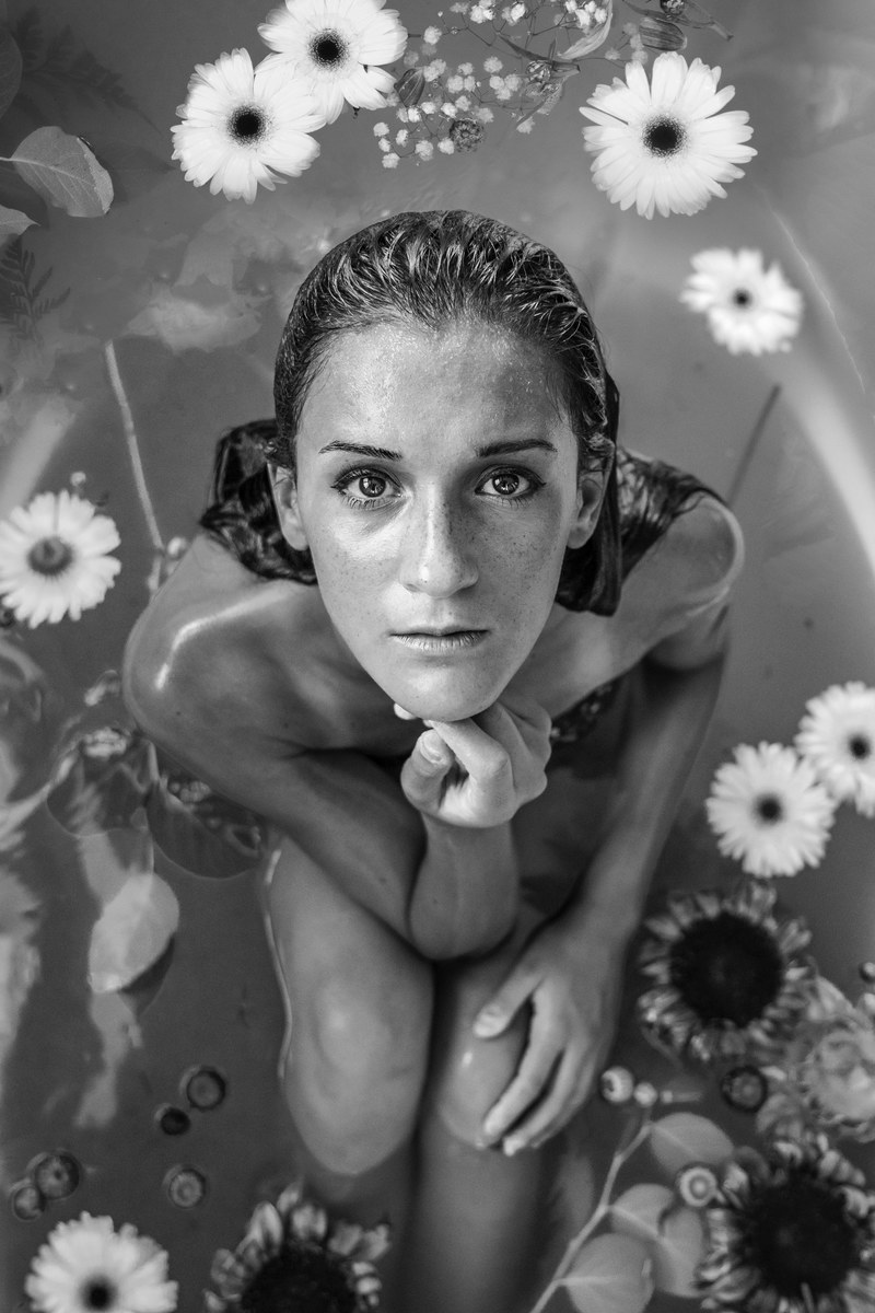 a black and white shot of a woman sitting in a bath filled with water and flowers, woman in flower bath in black and white 4k