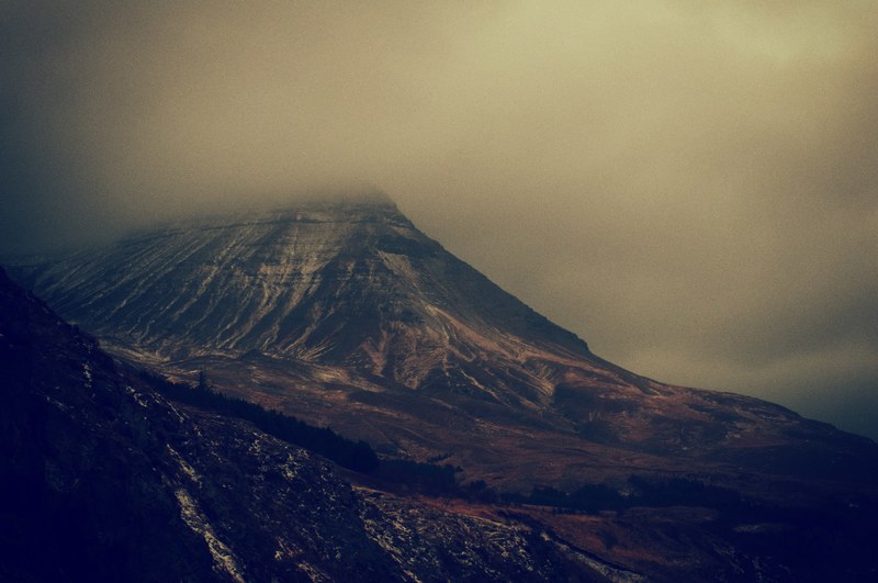 a somber shot of a massive mountain with its peak enveloped by clouds, towering mountain in the clouds 4k