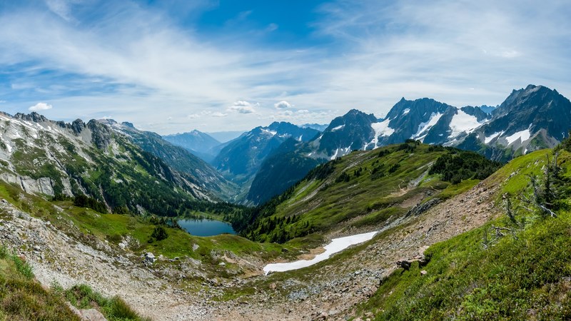 a green valley with a lake surrounded by jagged mountains with bright patches of snow, snow around a mountain lake 4k