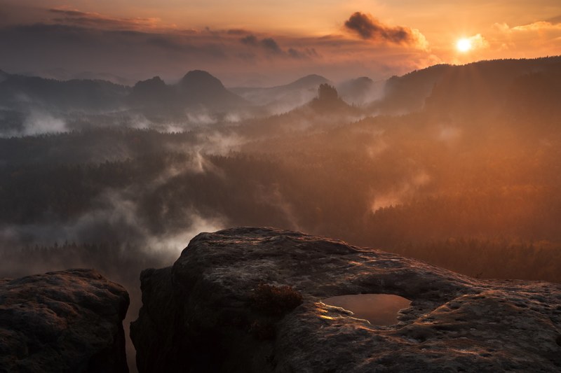 a puddle on a smooth rocky ledge overlooking foggy forests during sunset, sunrise at saxon switzerland 4k