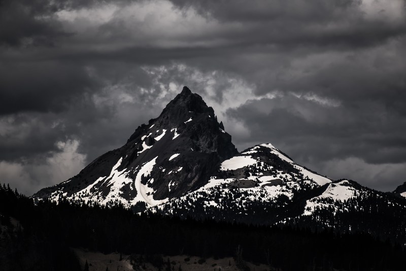 a desaturated shot of a dark mountain covered in patches of white snow under a gray sky, diamond peak in sepia 4k