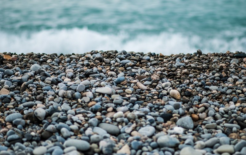 a low shot of a pebble beach with crashing sea waves in the distance, breeze over shingle beach 4k