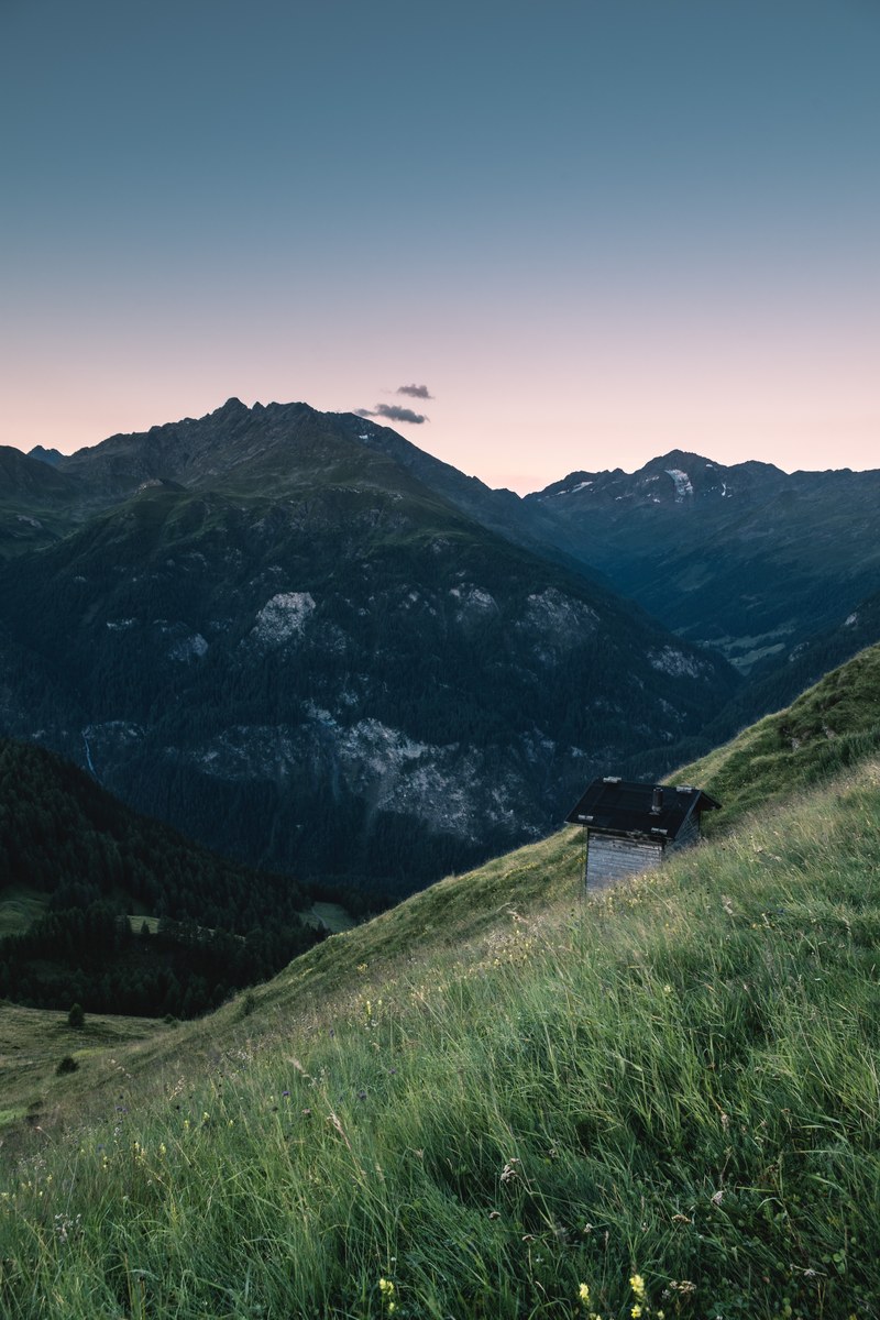 a small hut on a green slope in the alps, alpine hut in the evening 4k