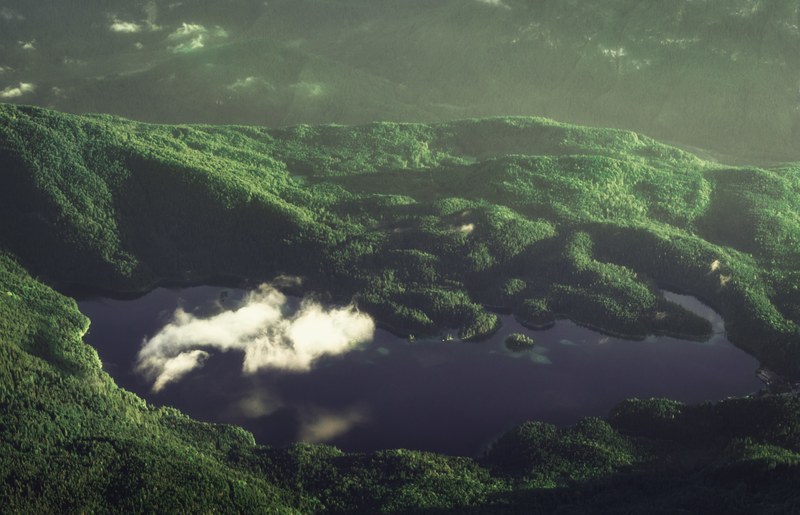 a drone shot of a small cloud over lake eibsee surrounded by green hills, cloud over a lake 4k