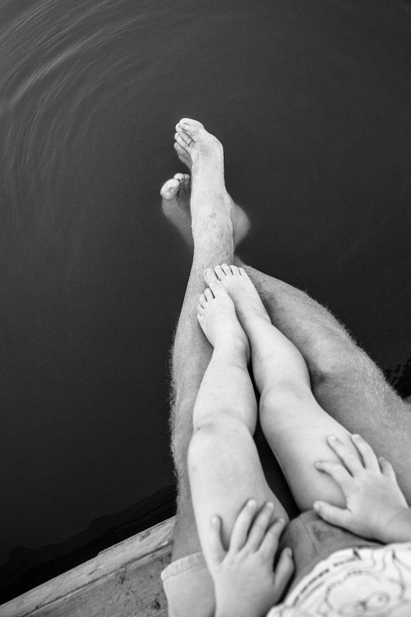 child sits on lap of parent as their legs dangle off into the water, summer waning 4k