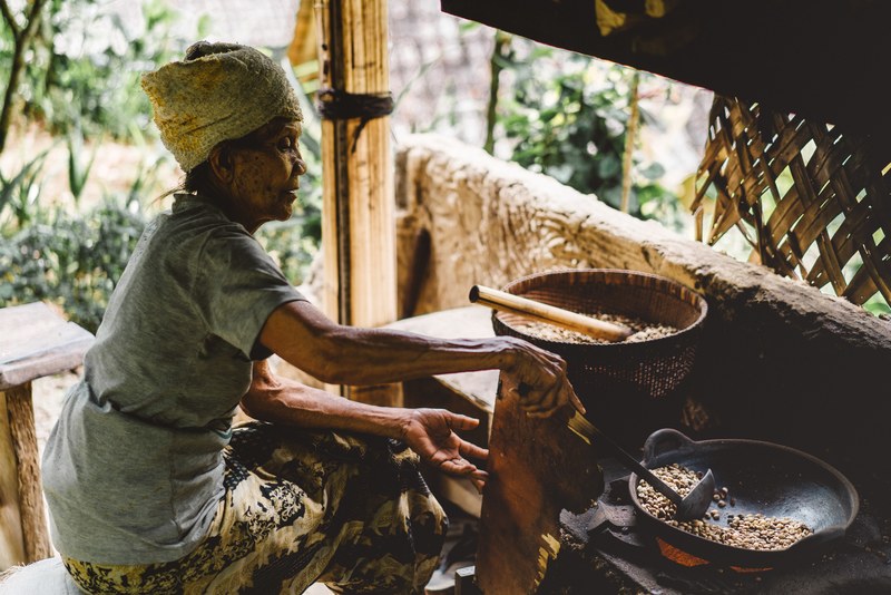 an old woman is sitting by the stove cooking beans with a spatula and a wok, _an elderly village woman cooking 4k