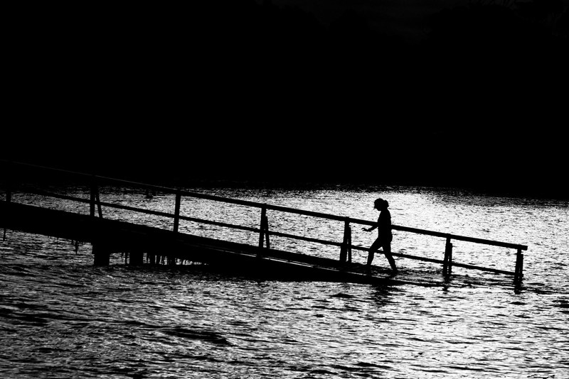 black and white shot of person walking in pier sinking into water, monochrome sinking pier 4k