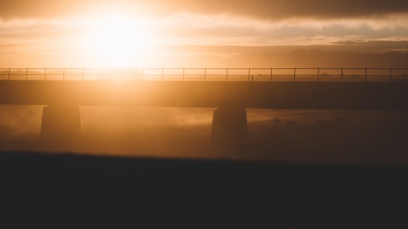 a hazy golden sunset puts a modern bridge into silhouette at rangitata river, rangitata river sunset_ 4k