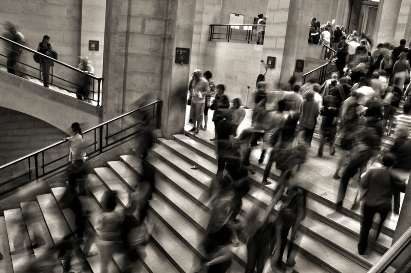 a desaturated long exposure shot of people crowding on stairs in a large public building, busy stairs in large building 4k