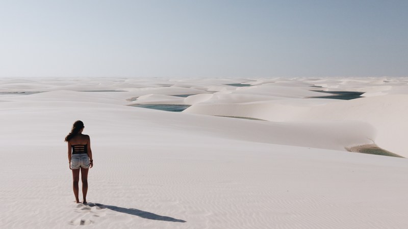 a woman walking in white sand with dunes nearby, _woman staring at sand dunes 4k