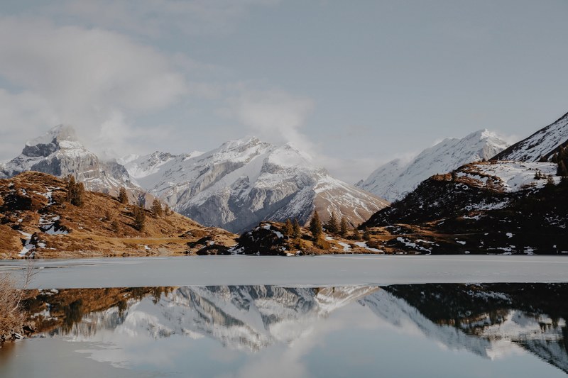 the half frozen surface of a lake near snowy mountain peaks in trbsee, the fight between fall and winter 4k