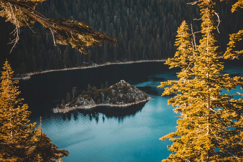 a drone shot of an island in the middle of lake tahoe surrounded by the forest, lake island in the autumn 4k