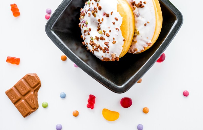 donuts with white frosting and pistachio nuts on top gummy bears sweets and a piece of a chocolate bar, sweet tooth 4k