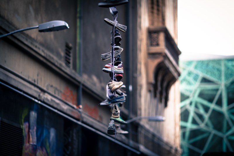 multiple sneakers lace tied together hanging from streetlight as tribute in decaying urban area hosier lane, sneakers hang over street 4k