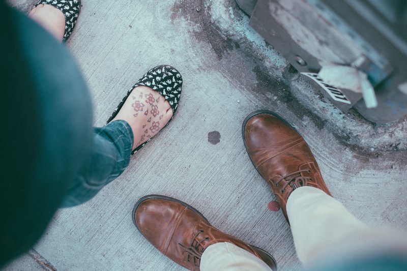 man wearing brown boots and woman with flower tattoos on her feet wearing patterned flats in williamsburg, shoes with different styles 4k