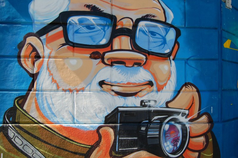 a wall mural of an old man with a white beard and hair holding a camera, _old man camera graffiti 4k