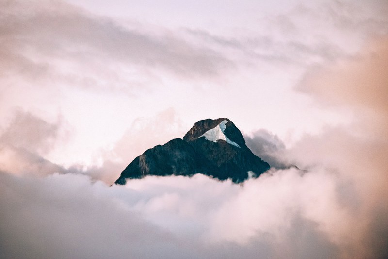 a granite mountain peak rising up above pink hued clouds, mighty peak above clouds 4k