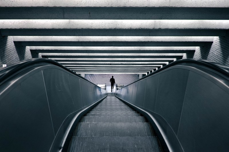 person gets off an escalator inside a gray industrial building, escalator lines and shadows 4k