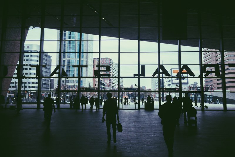 passengers are at the entrance of the rotterdam centraal station with the rotterdam cityscape in view, _silhouettes rotterdam station 4k