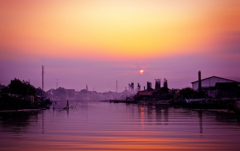 buildings and boats on the rippling river with a purple and orange sunset sky overhead semarang city, purple and orange sunset over the river 4k