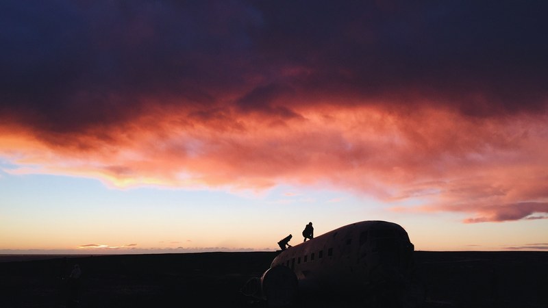 two people climbing on an abandoned airplane under a sunset sky with pink clouds in solheimasandur, pink clouds in a solheimasandur sunset 4k