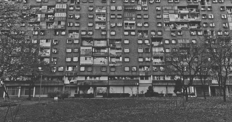 black and white shot of rundown residential building with grass and trees in novi beograd, belgrade brutalism 4k