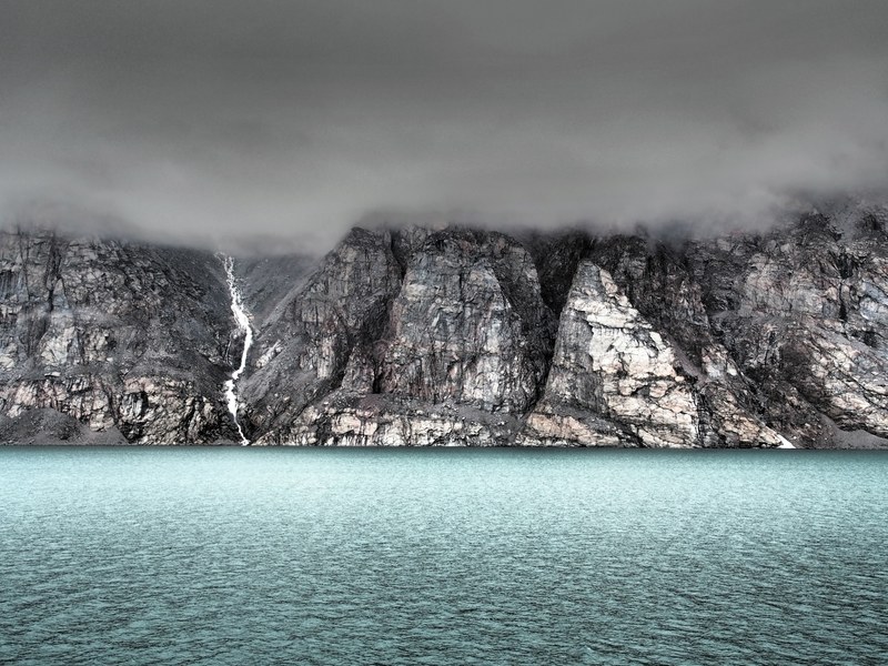 storm rolls in over rocky cliffs near blue waters in baffin island, stormy mountain sky 4k