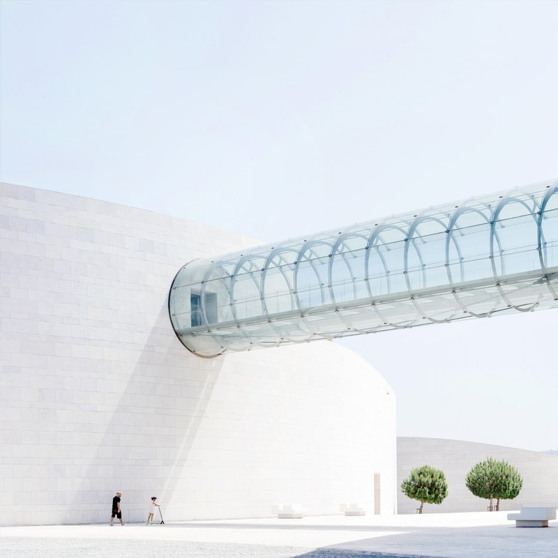 two people under a cylindrical glass skyway connecting two buildings, fundaco champalimaud 4k