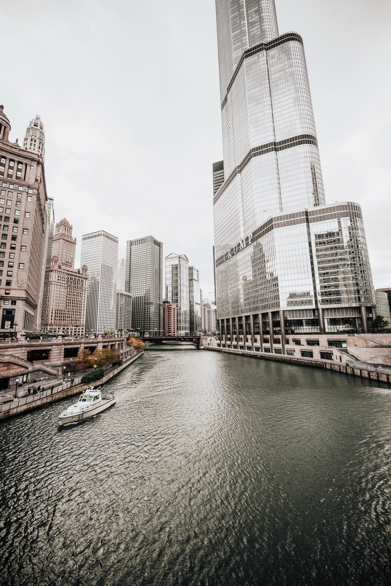 a pale shot of the chicago river with a boat on it next to a skyscraper, chicago 4k