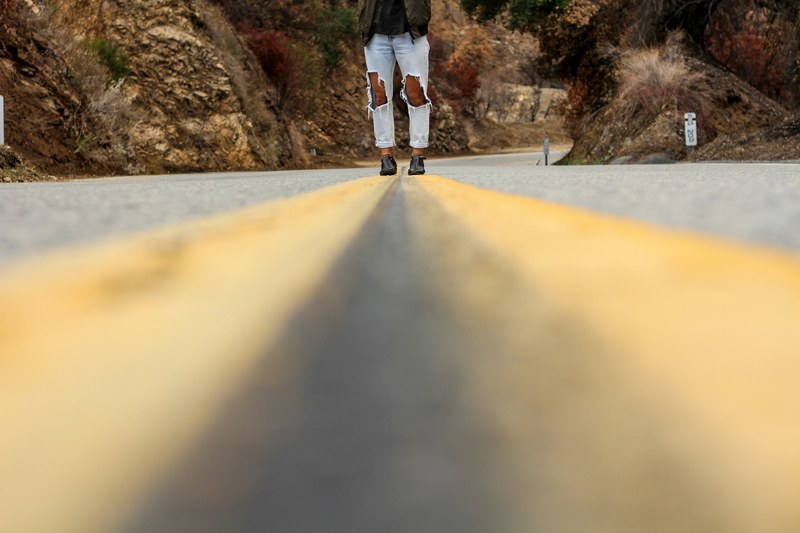 a person in ripped jeans standing in the middle of an empty road through a canyon, ripped jeans on the road 4k