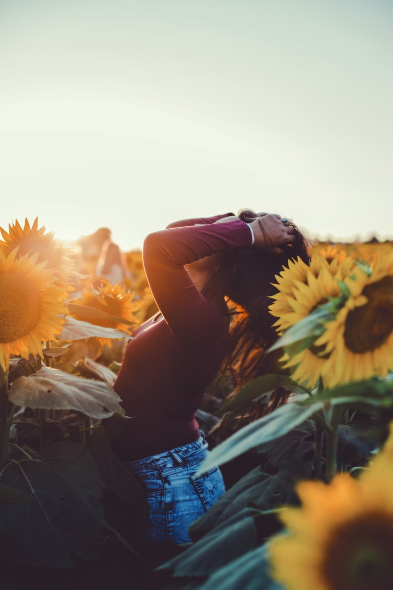 a woman wearing jeans and a sweater standing in a sunflower field at grinter sunflower farms, sunset 4k