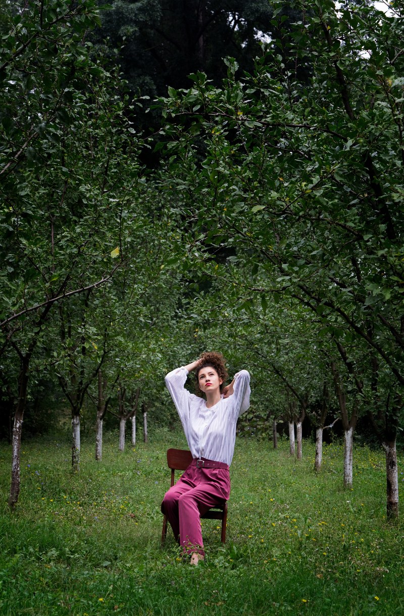 fashionable woman sitting in a chair in a tree orchard, orchard outfit 4k